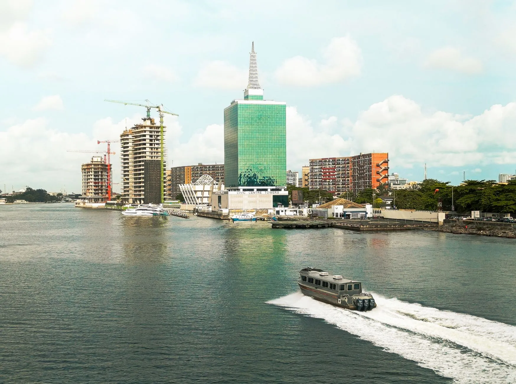 Scenic view of Lagos skyline featuring modern buildings and a motorboat in the lagoon under a bright sky.