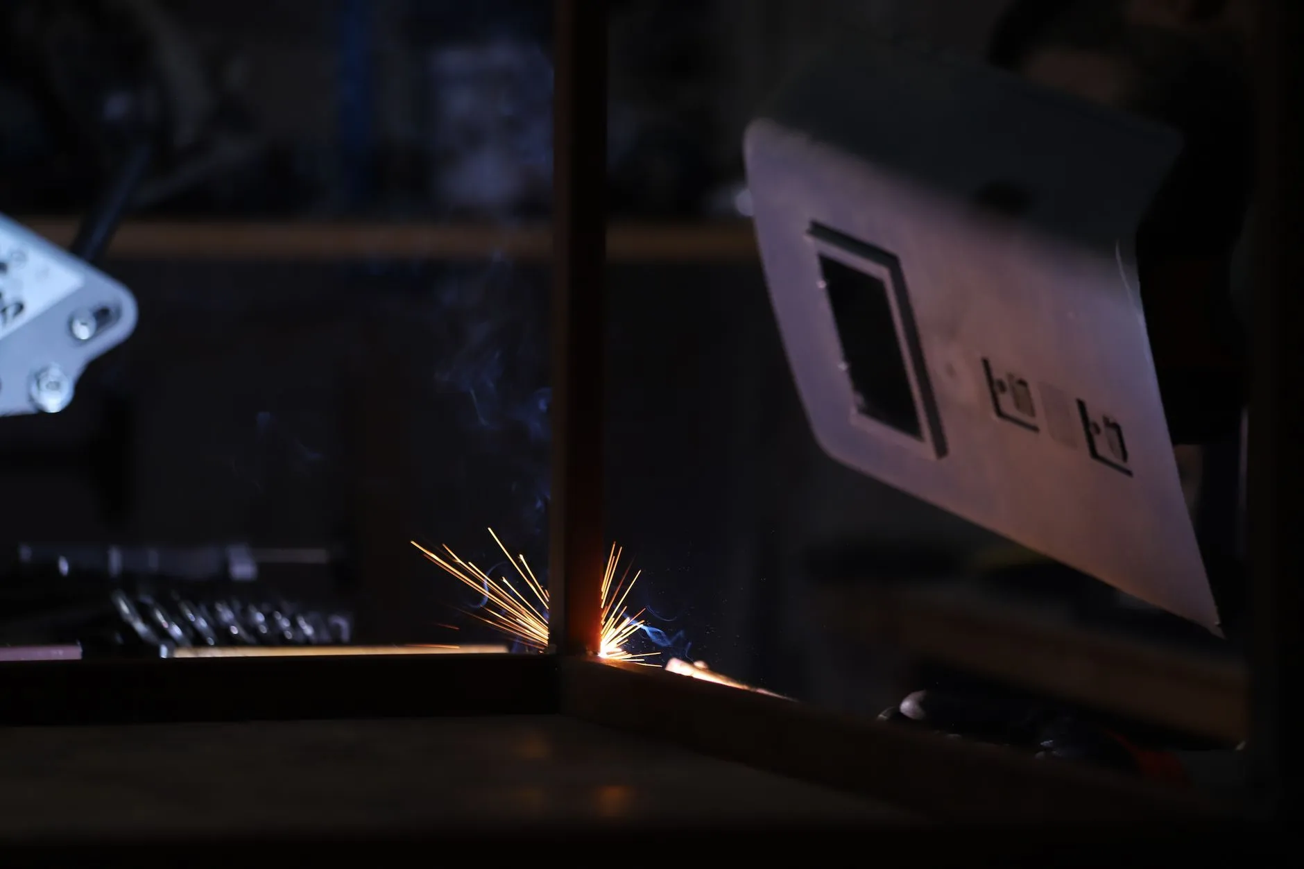 Close-up of a welding process in a dark workshop showing bright sparks and protective gear.