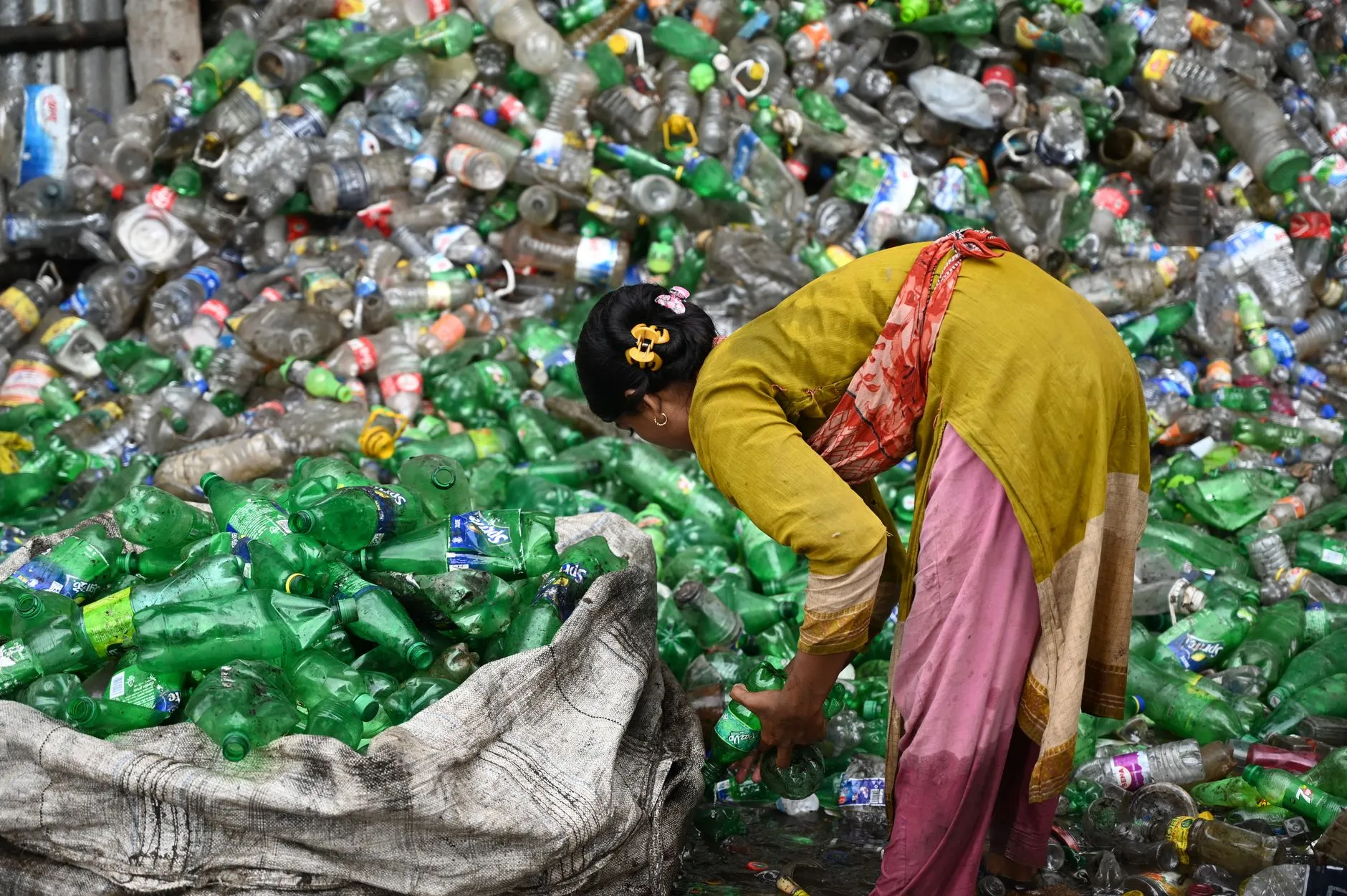 Woman collecting and sorting plastic bottles for recycling in Chattogram, Bangladesh.